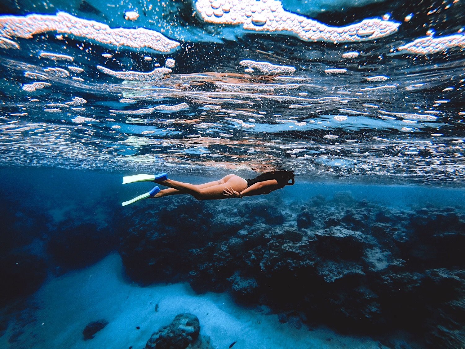 Underwater view of a snorkeler swimming through clear blue waters near rocky formations.