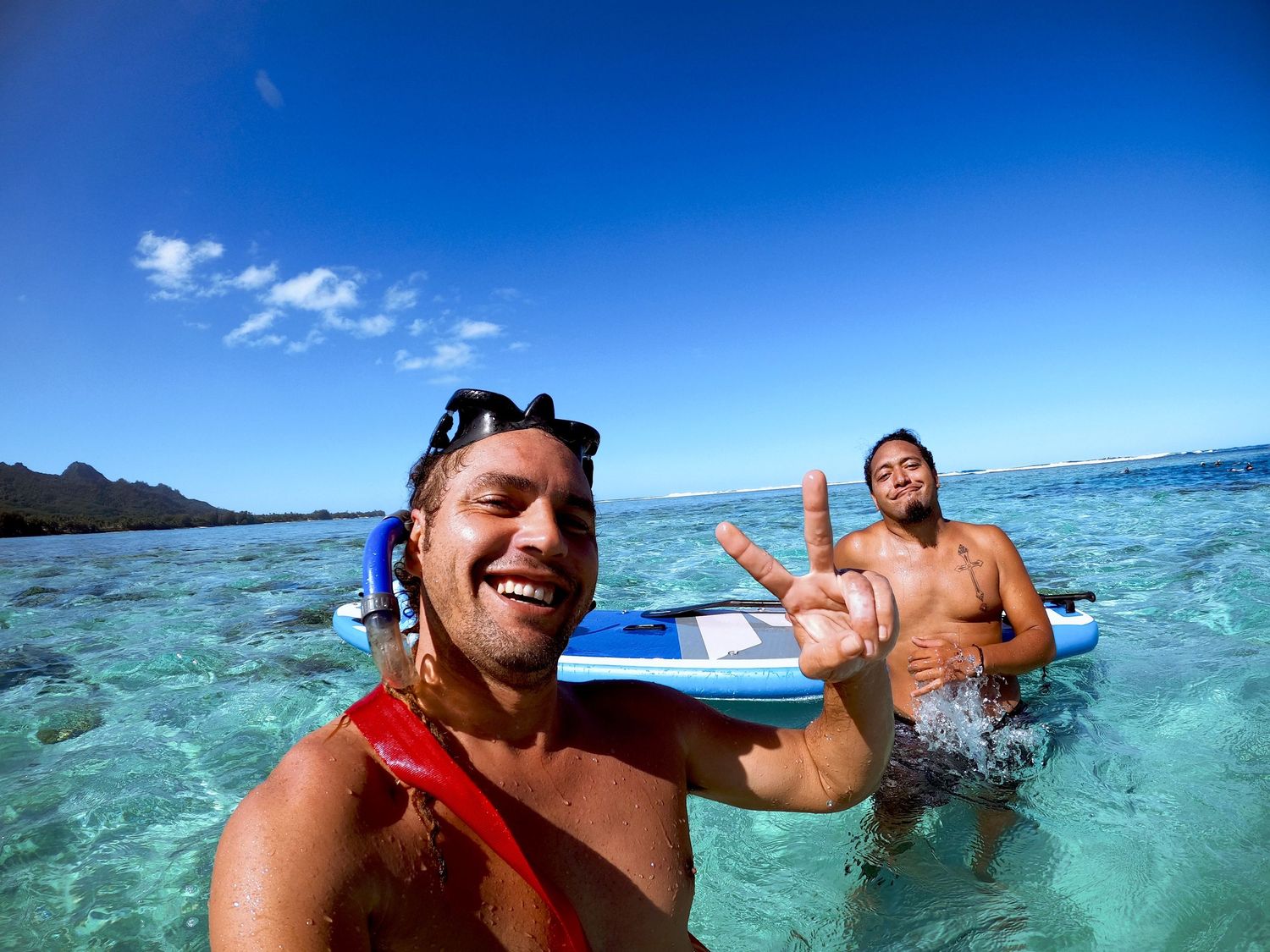 Snorkelers enjoying crystal clear tropical waters with reef visible in background.