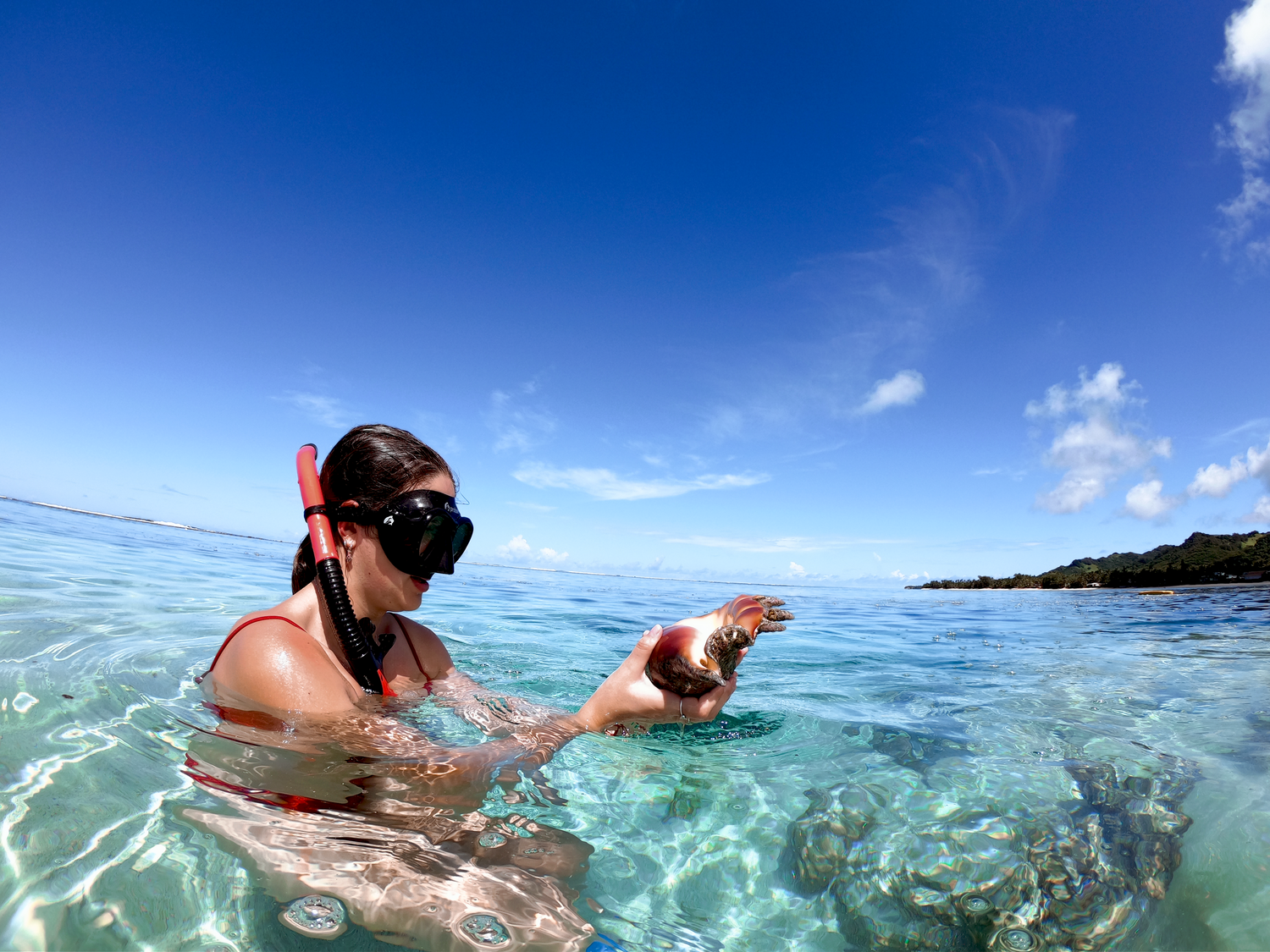Snorkeler points while swimming in crystal clear tropical waters on a sunny day.