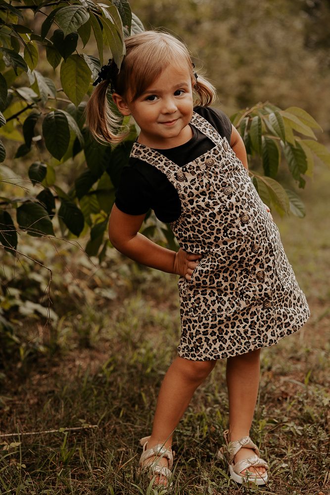 Young child in leopard print outfit plays and poses playfully in an outdoor garden setting.