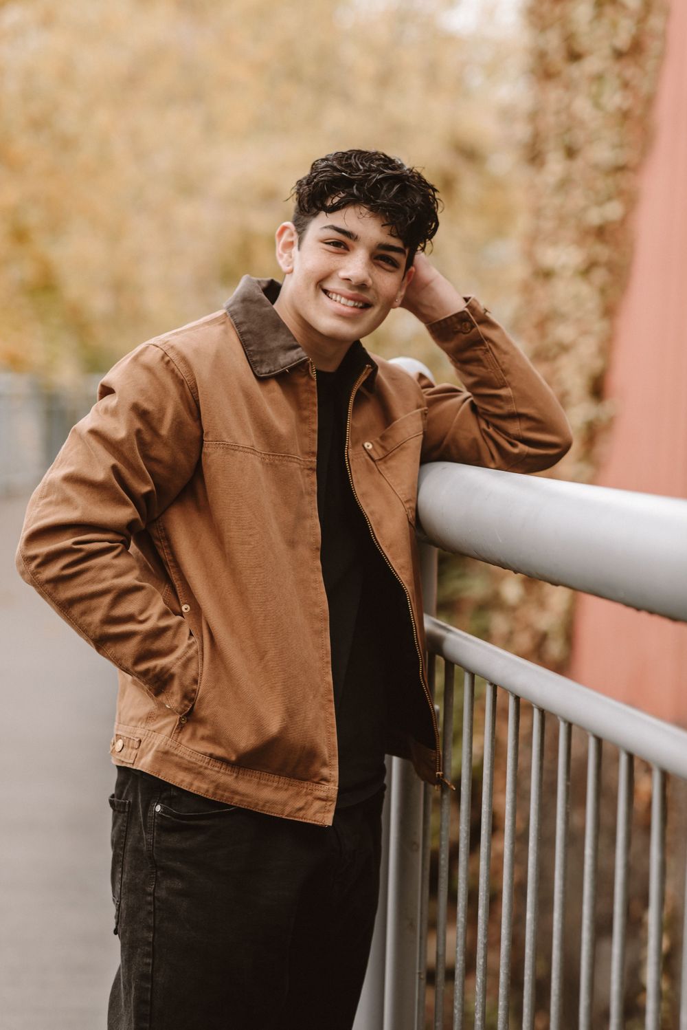 Casual portrait series against pink wall with metal railing during autumn season.