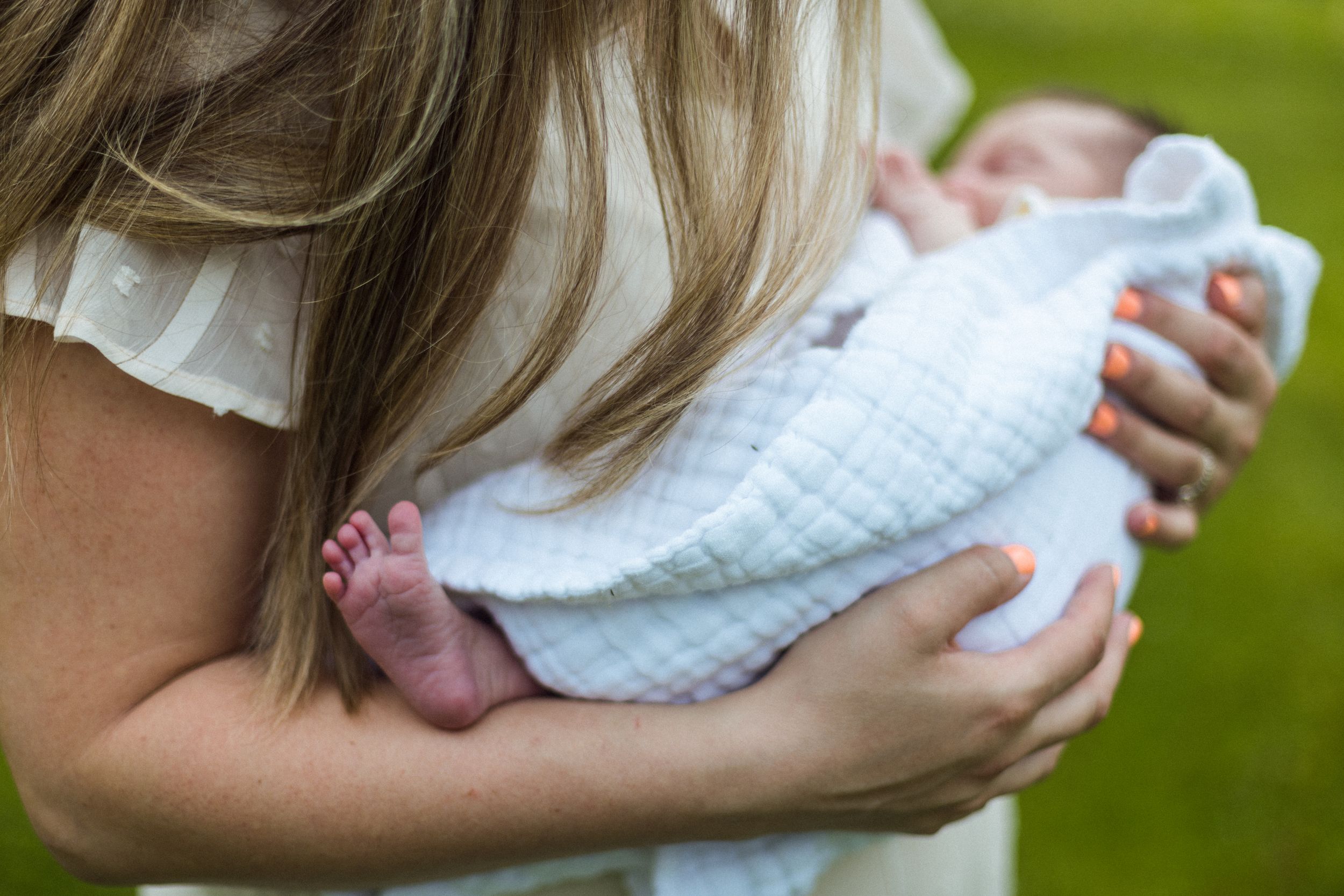 Tiny newborn baby feet peek out from a white blanket held in gentle arms.
