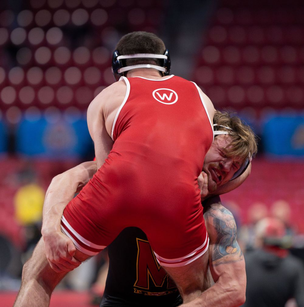 Wrestling competition match between two athletes in red and black uniforms.
