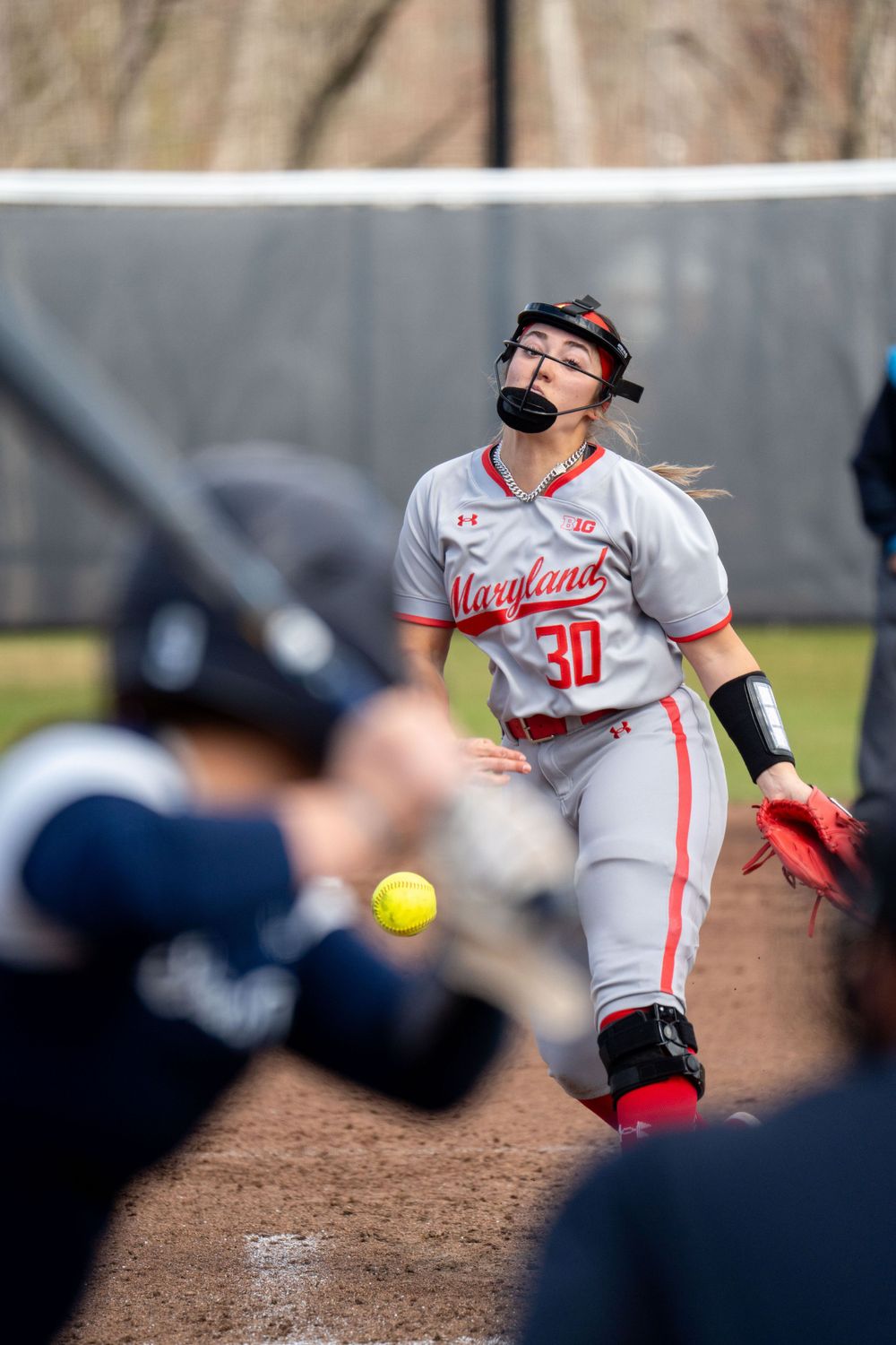 Softball pitcher in mid-delivery motion wearing gray uniform with red accents.