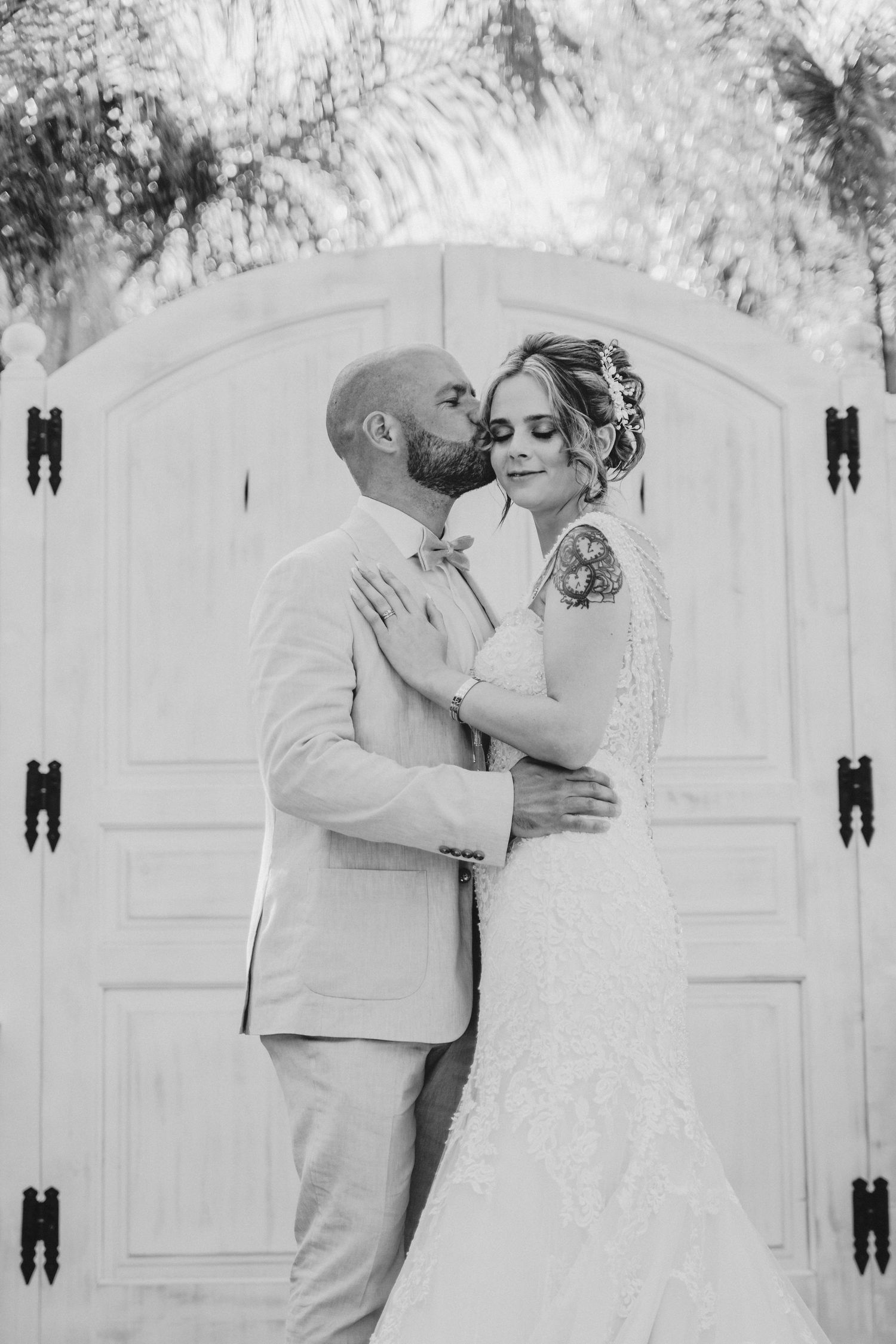 Black and white wedding portrait of couple embracing in front of elegant white doors.