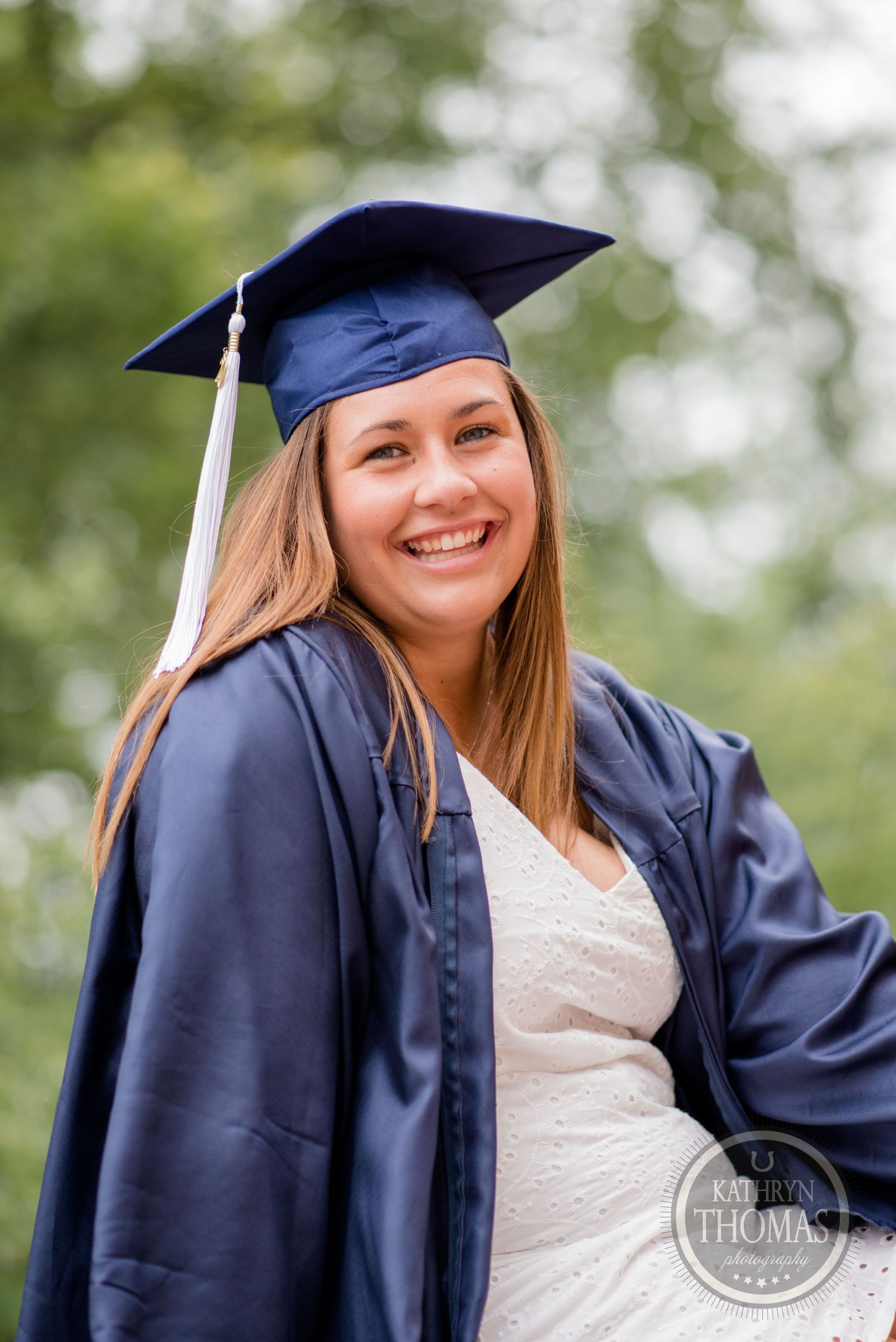 Graduate wearing blue cap and gown smiles outdoors on graduation day.