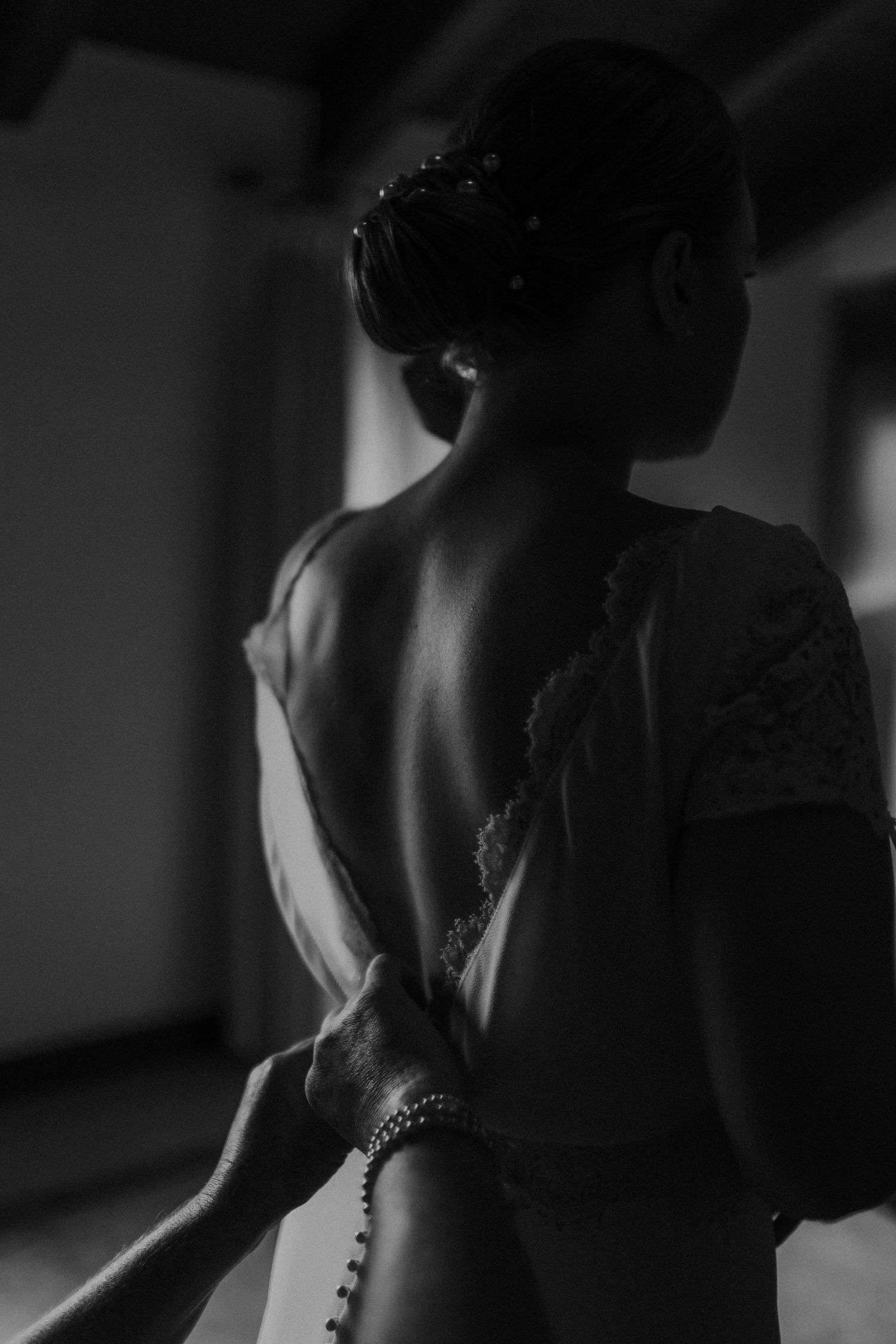 Artistic black and white photo showing the back of a wedding dress with buttons and lace details.