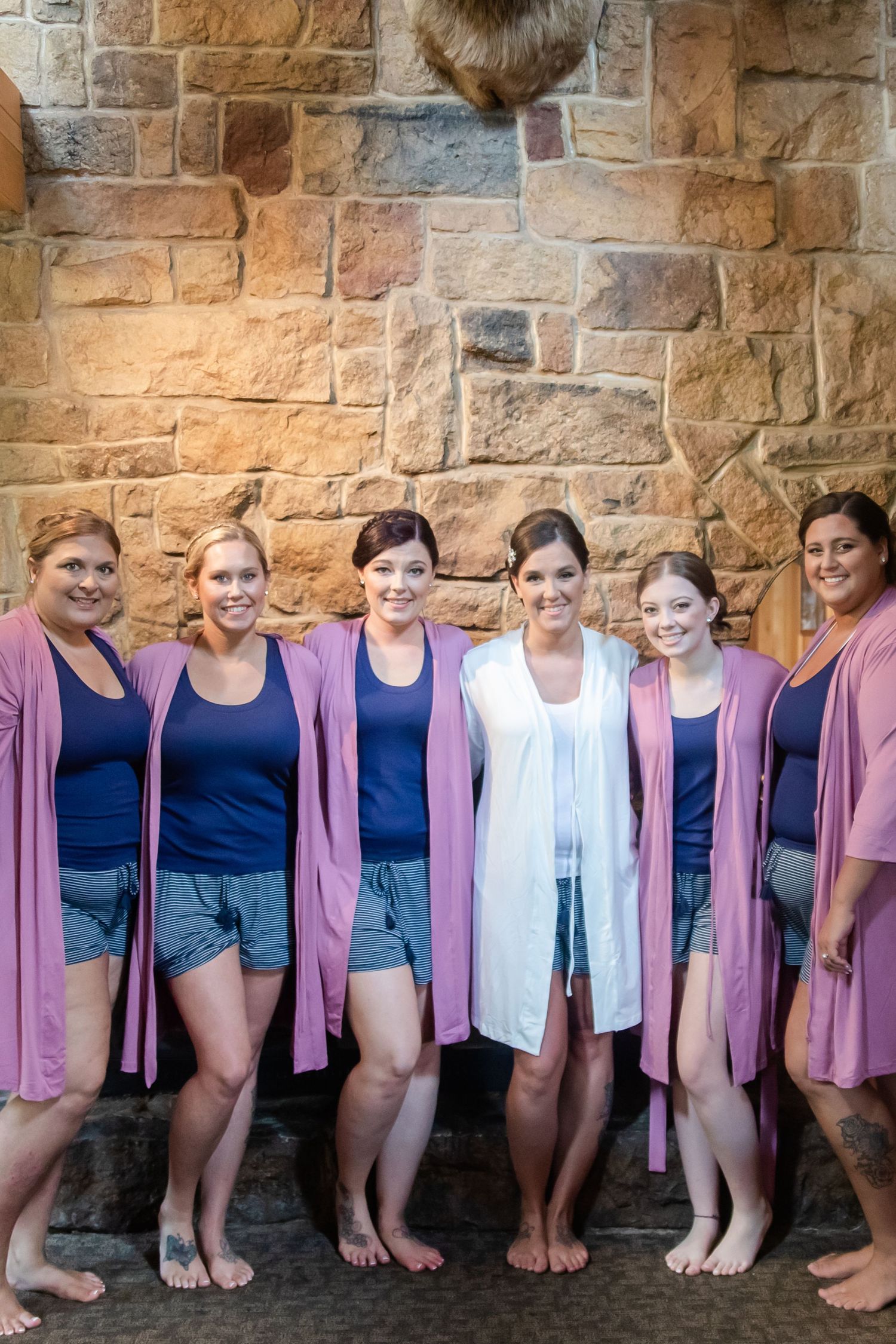 Bridal party in navy dresses and pink cardigans poses against a stone wall.