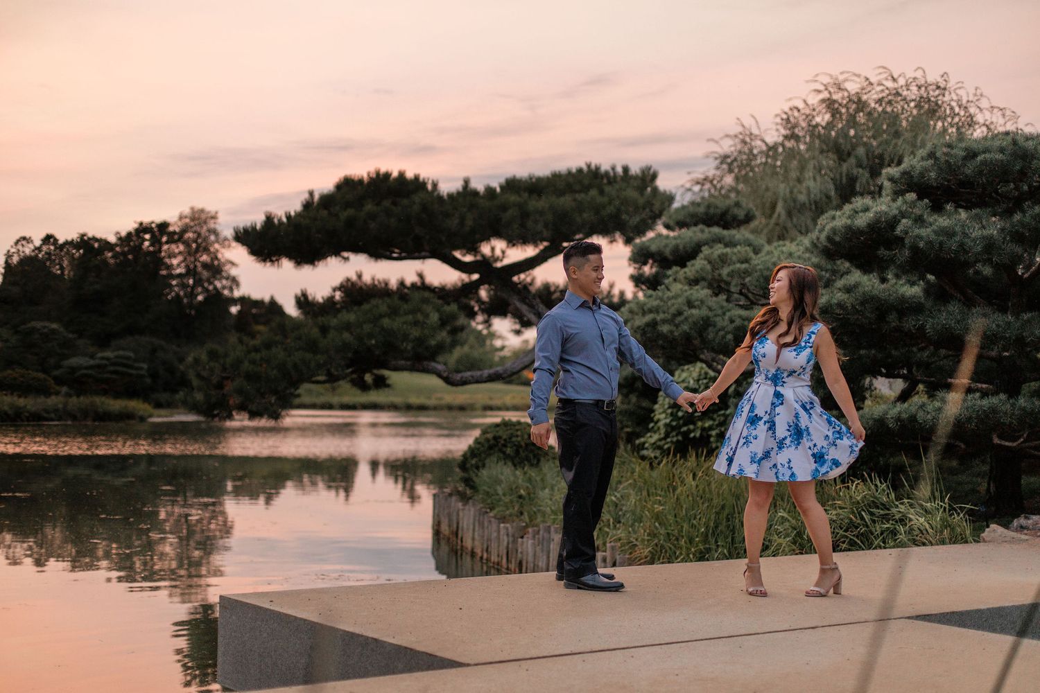 A couple dances together by a lake during sunset in a romantic garden setting.
