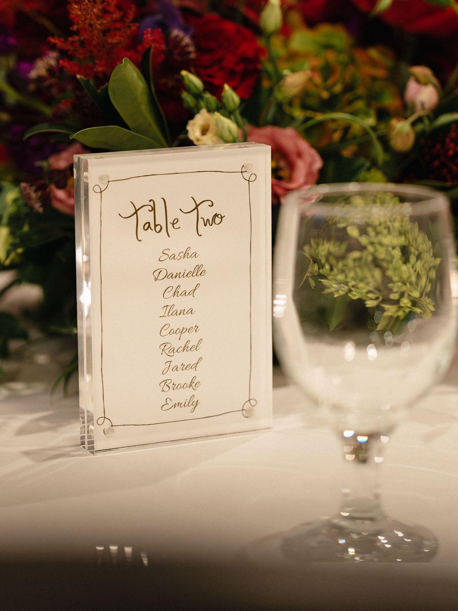 Elegant table number card listing guest names surrounded by floral decorations.