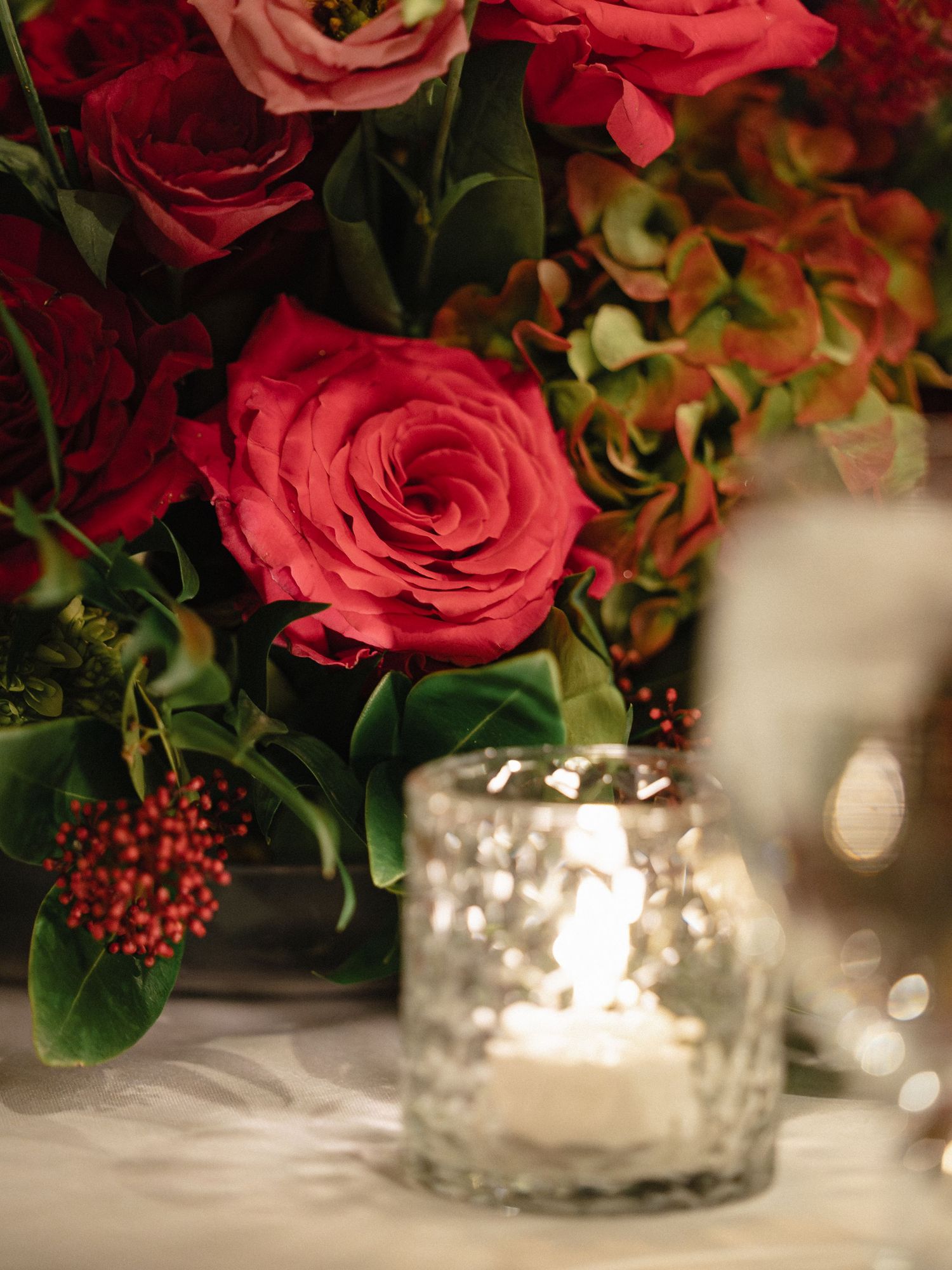 Beautiful red roses and greenery arrangement with glowing candle centerpiece.