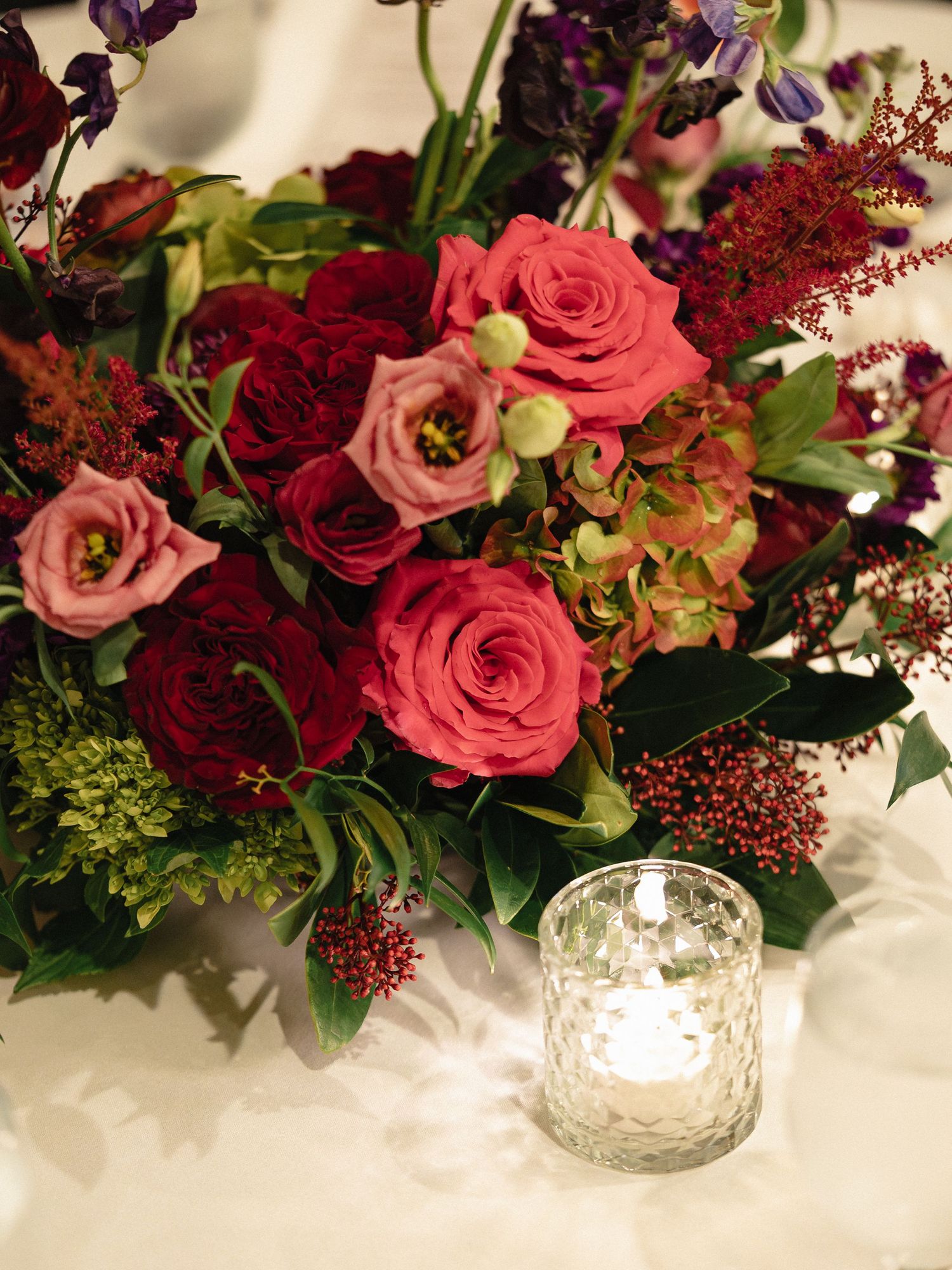 Beautiful floral centerpiece with pink and red roses alongside decorative candle holder.