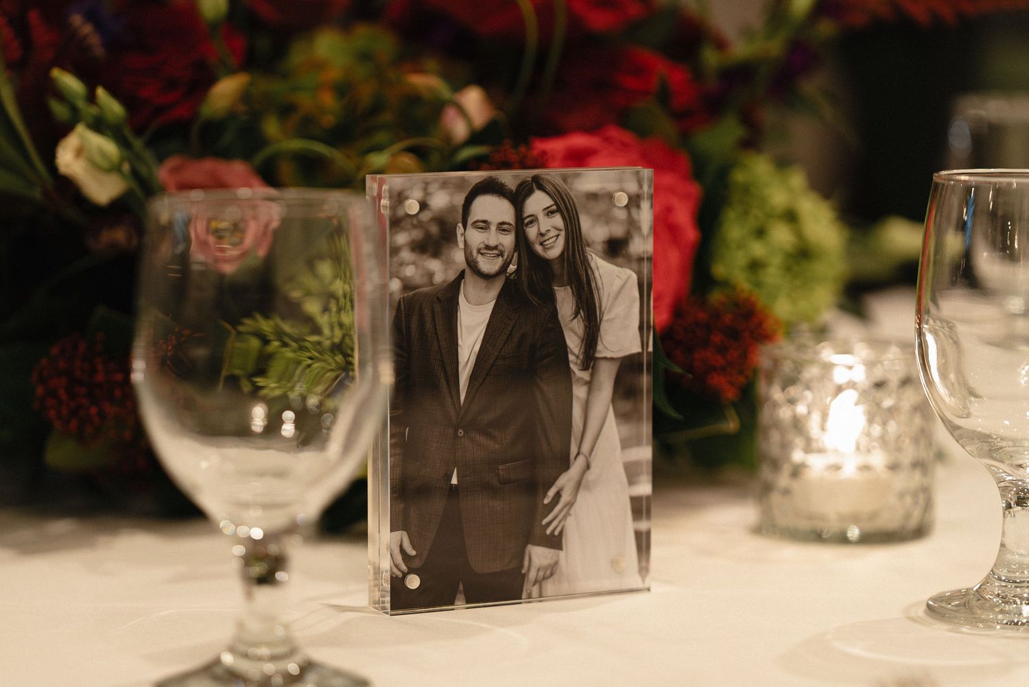 Black and white photo displayed on elegant table with flowers and glassware.