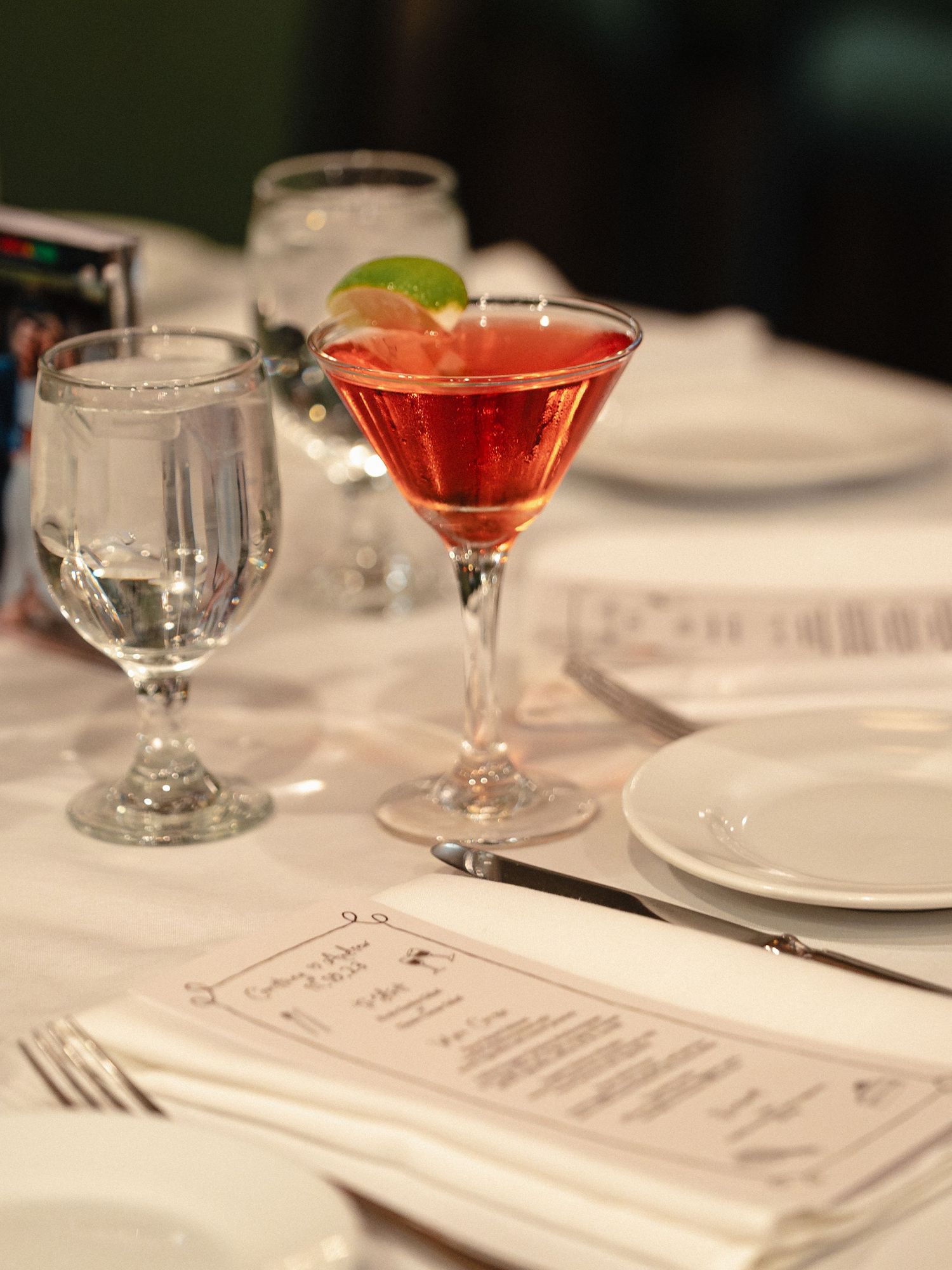 Red cocktail and place settings on elegant white tablecloth with menu card.