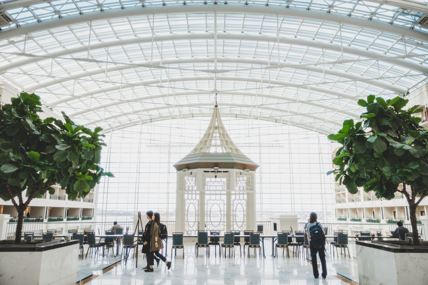Modern atrium with glass ceiling, gazebo centerpiece and indoor trees.