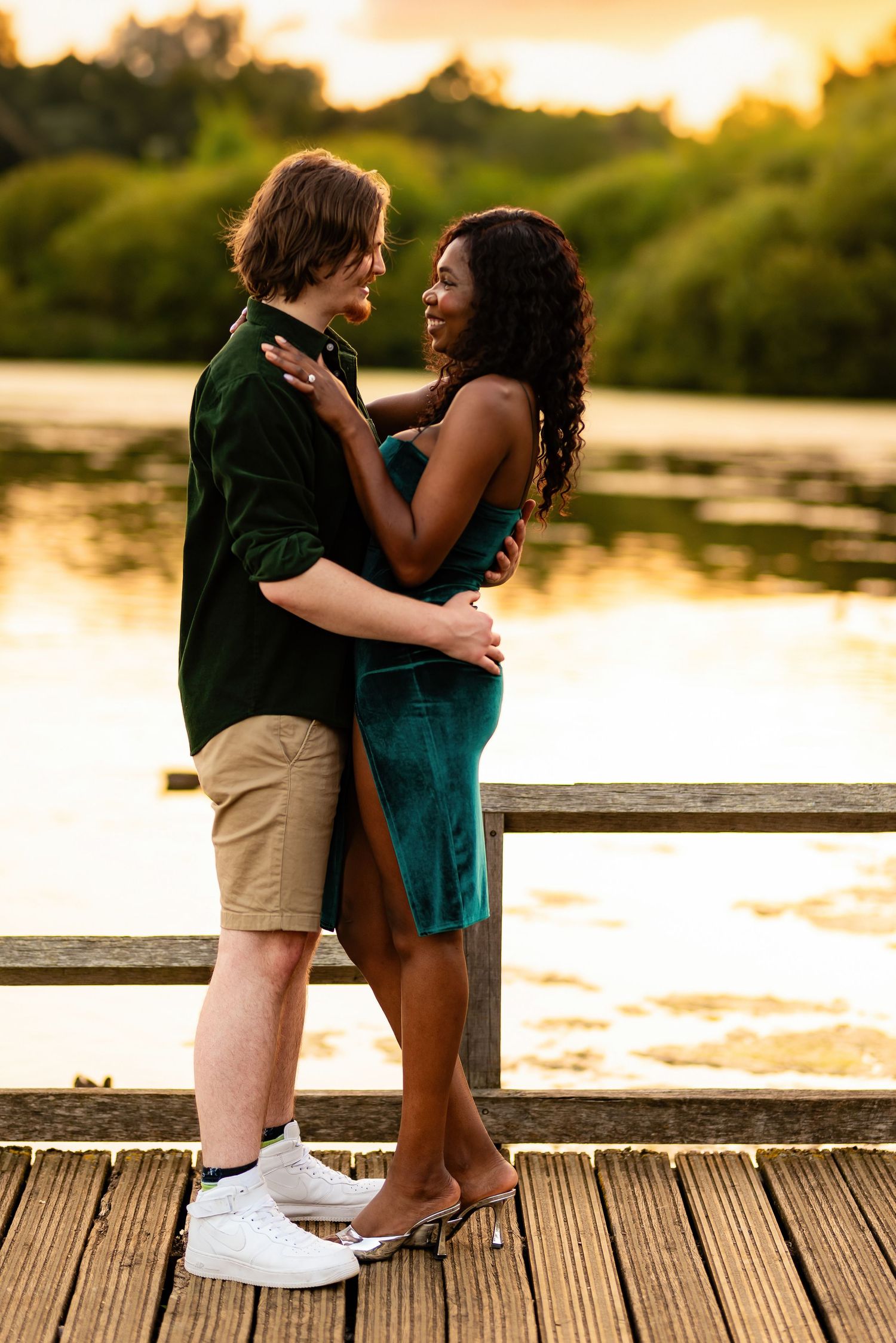 Couple embracing on wooden dock during golden sunset by a tranquil lake.