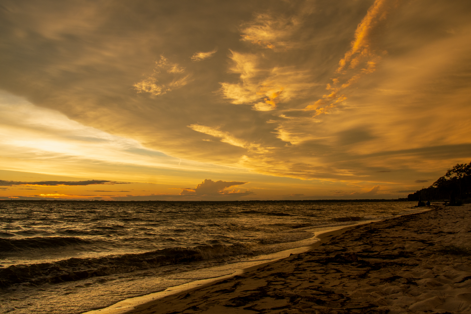 Dramatic golden sunset over ocean beach with vibrant orange clouds reflecting on water.