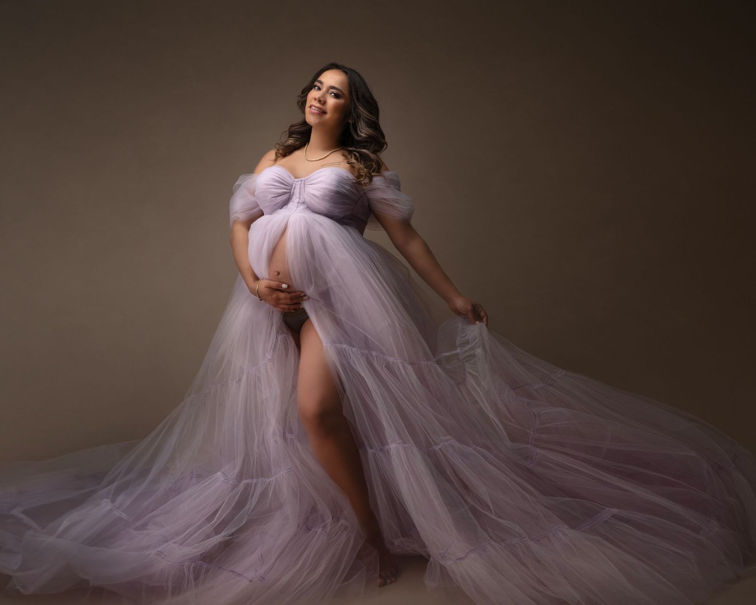 Ethereal maternity portrait with billowing lavender tulle dress against dark background.