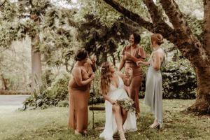 Wedding party gathers under a large tree for outdoor group photos.