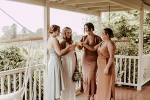Wedding party in neutral tones poses together on a white porch during an outdoor celebration.