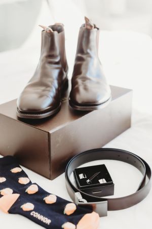 Wedding accessories including brown leather dress shoes and a black belt arranged on dark surfaces.