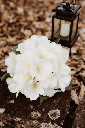 Delicate white flowers arranged with a black lantern on a rustic surface create an elegant wedding decoration.