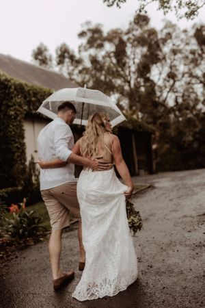 A couple shares a romantic moment under an umbrella on a rainy wedding day.