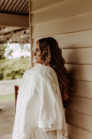 A detailed view of a white wedding dress with pearl embellishments hanging against a cream wall.
