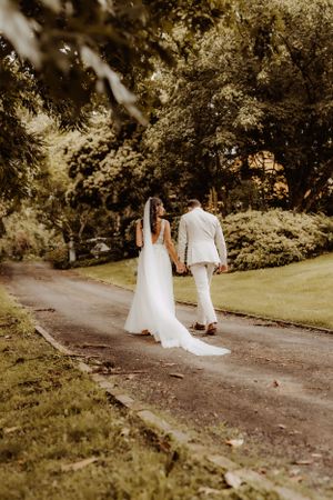 A couple in wedding attire walks down a winding garden path together.