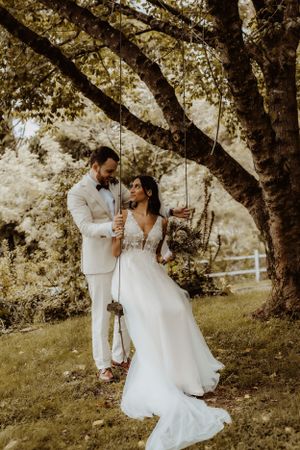 Romantic couple on tree swings in a dreamy outdoor setting wearing wedding attire.