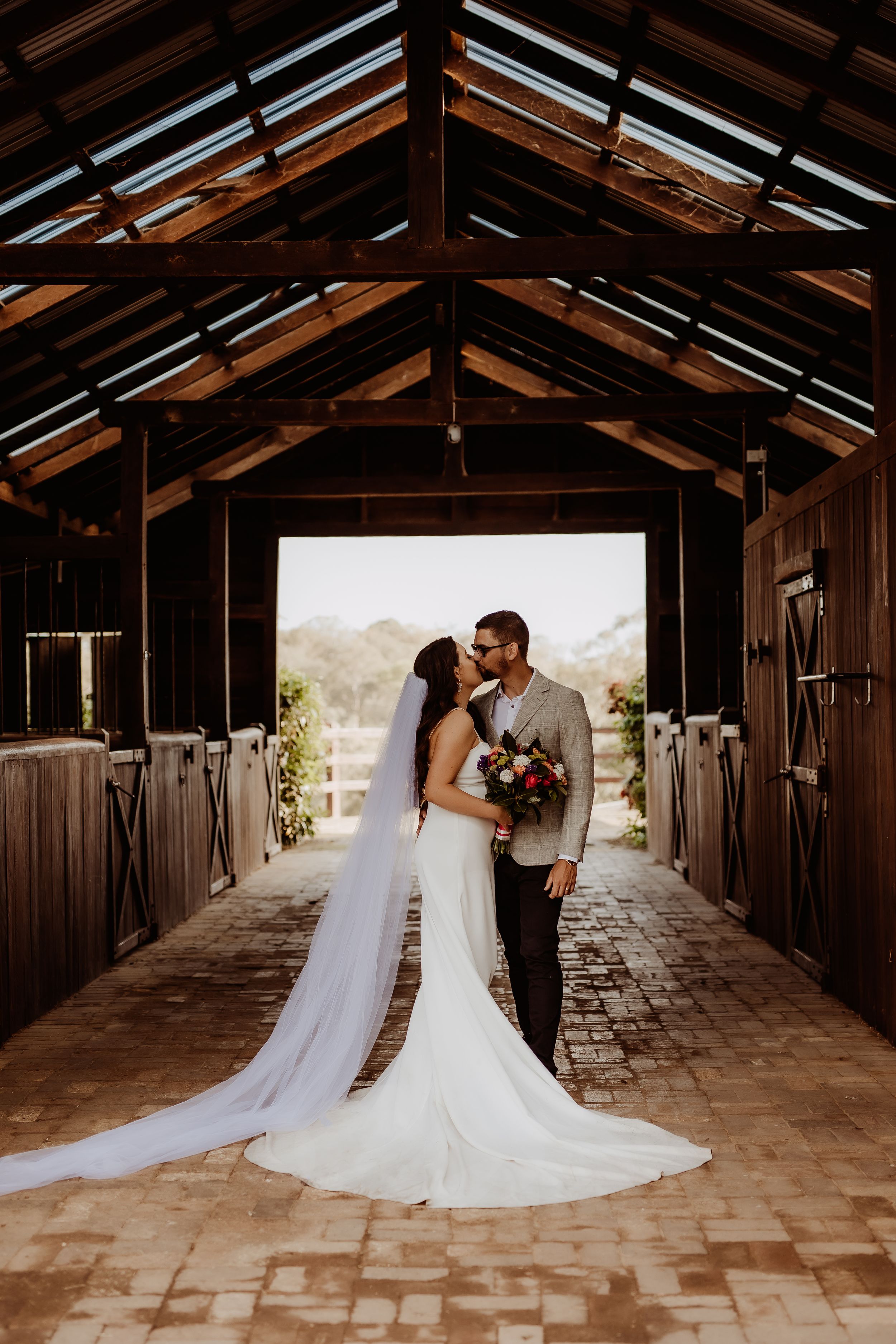Wedding couple in rustic wooden barn with dramatic lighting and brick floor.