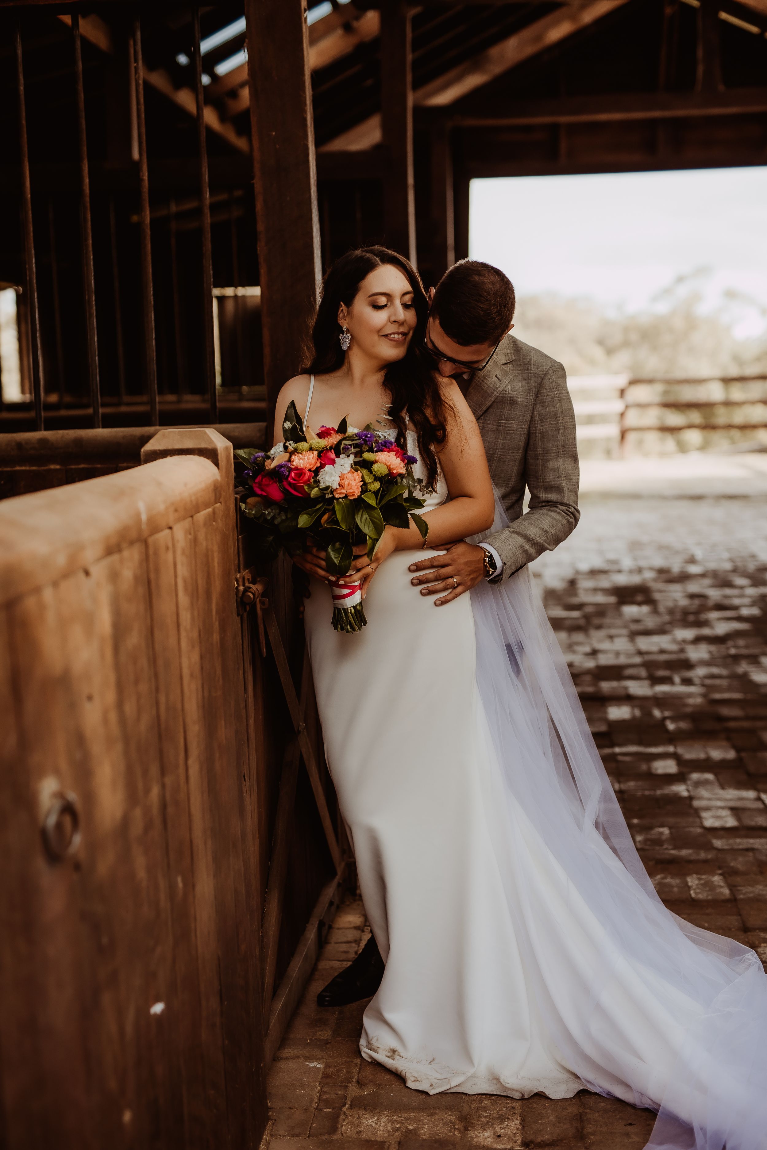 Wedding couple poses intimately in a rustic barn setting with soft natural lighting.