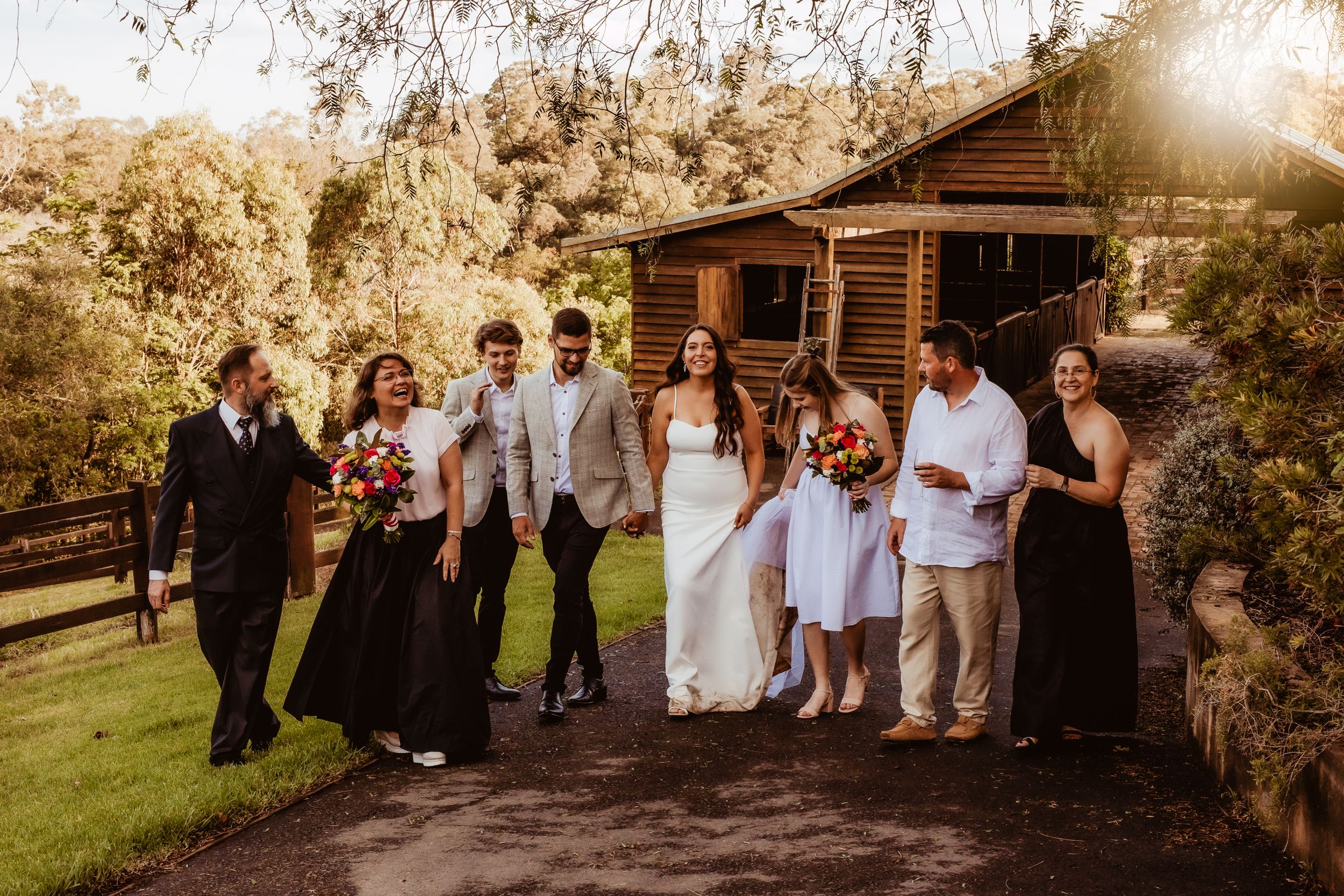 Wedding party gathered outside rustic venue for group photo.
