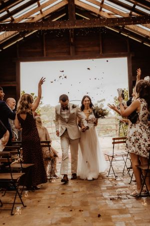 Wedding guests throw confetti during a joyous celebration in a rustic covered venue.