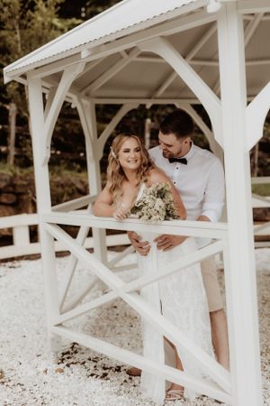 A joyful wedding moment captured under a white wooden gazebo with natural lighting.
