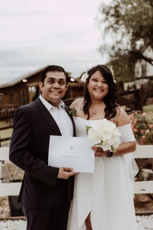 Wedding couple exchanging letters and smiles while holding white bouquet.