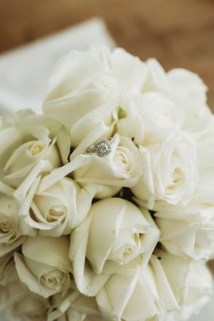 A delicate bouquet of white roses with a diamond engagement ring nestled among the petals.