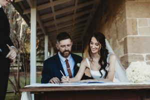Couple signing marriage documents under a rustic covered porch.