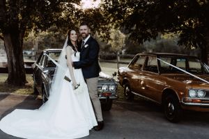 Wedding couple posing near vintage cars during golden hour photography session.