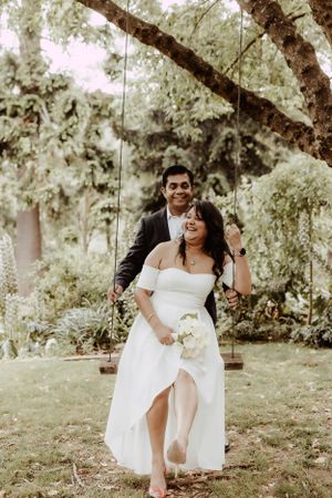 Playful wedding couple laughing together in sunlit garden setting.
