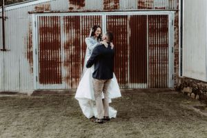 Wedding party laughing together in front of weathered metal building wall.