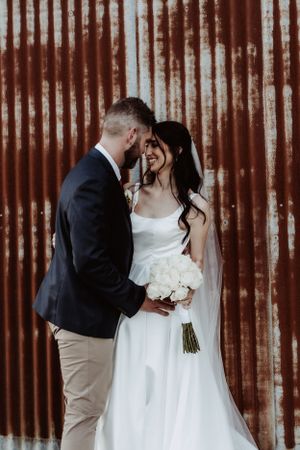 Intimate wedding moment captured against rustic red metal wall backdrop.