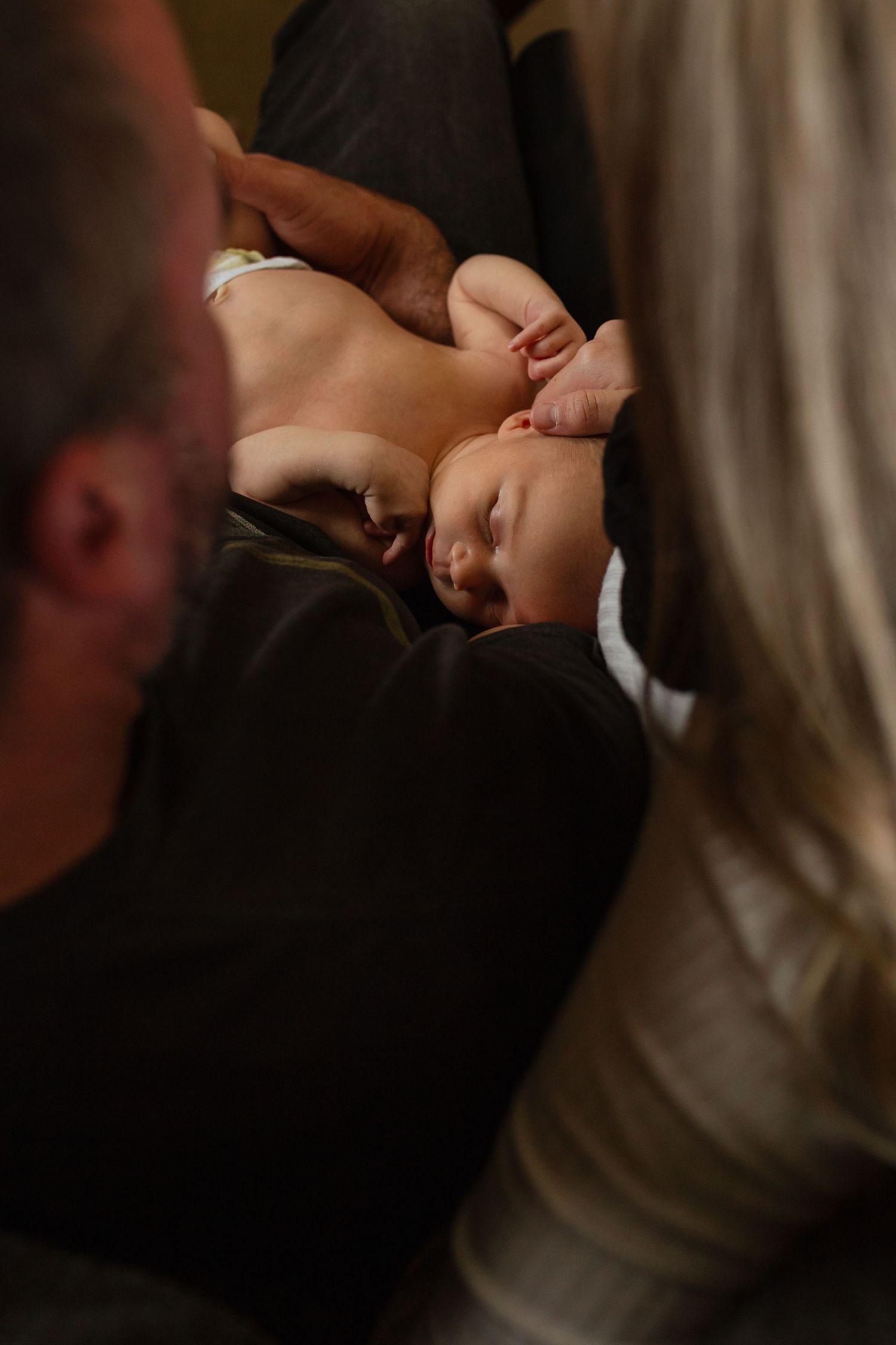 Newborn resting on parents' laps, viewed from behind