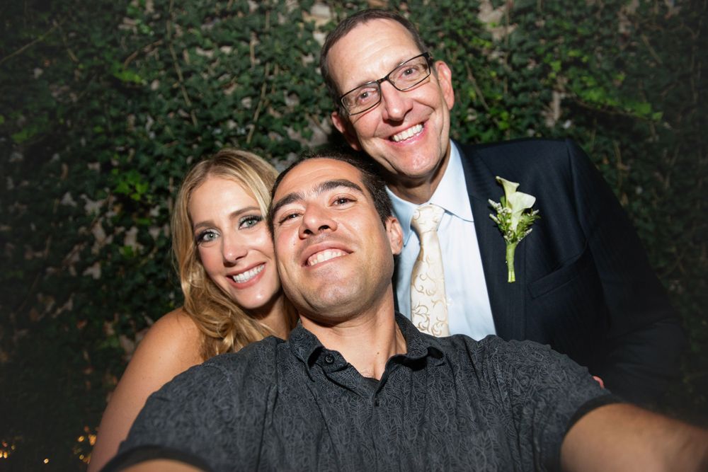 Three people pose together for a fun selfie at what appears to be a wedding celebration.
