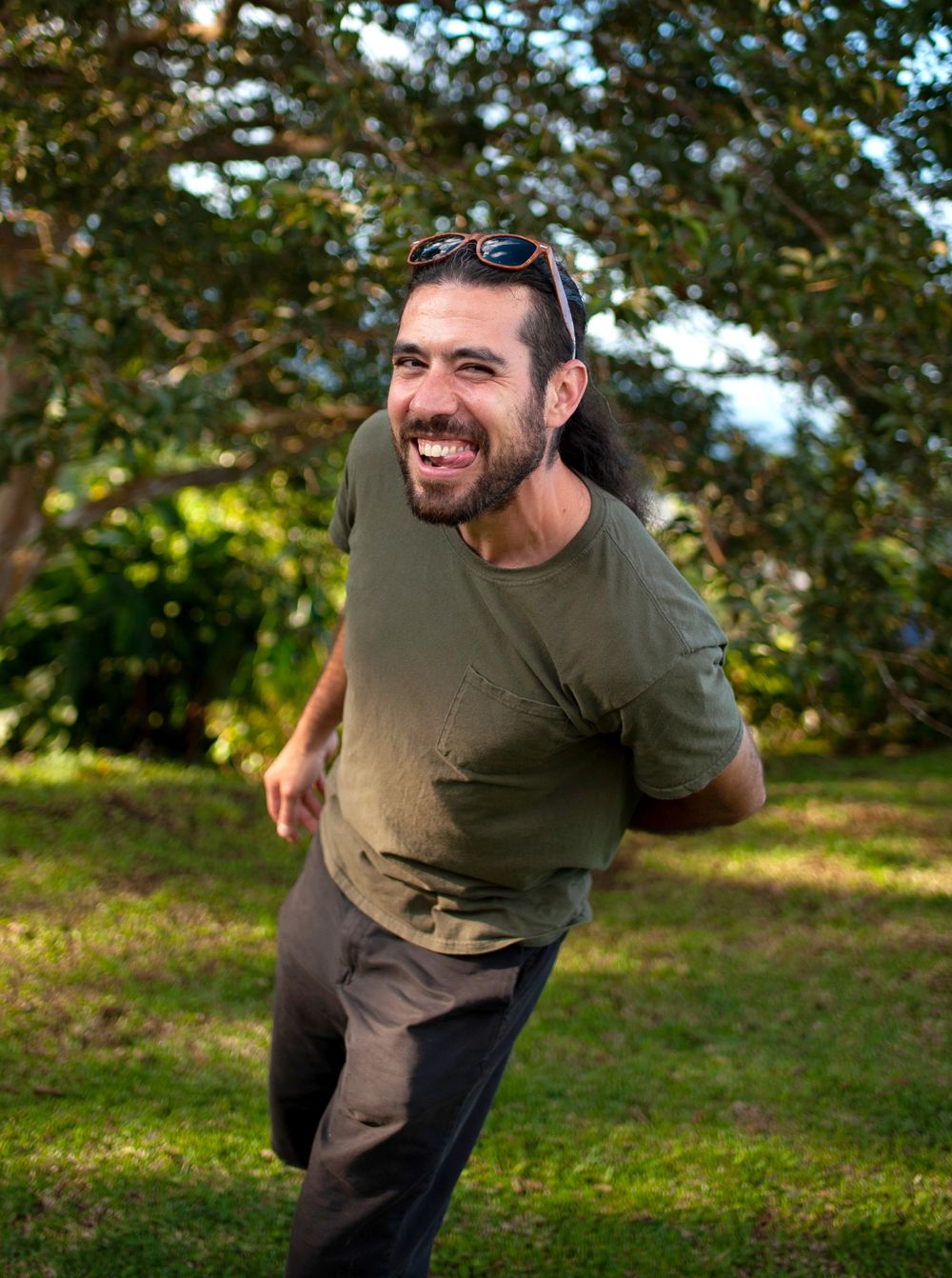 Carey Primeau standing and making a silly face with green grass and trees in the backgroud atop a hill in Costa Rica.