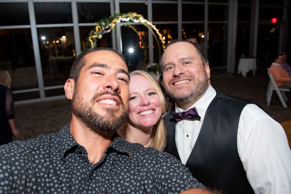 Three people pose for a close-up photo under decorative lighting at an event.