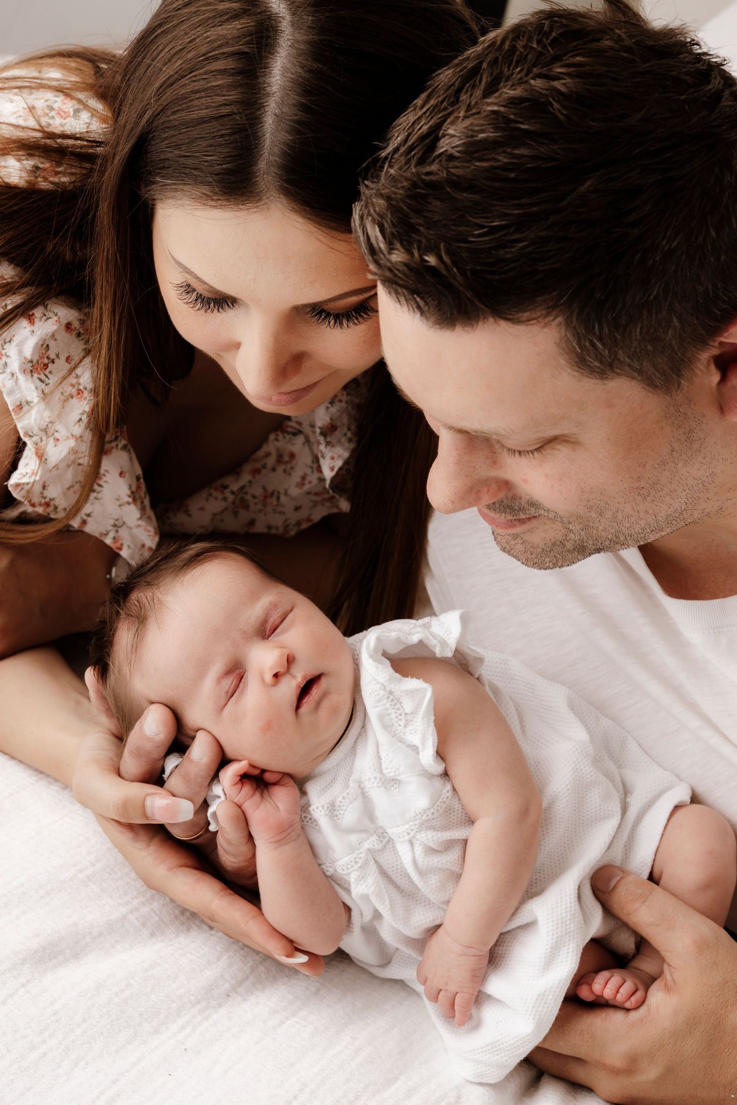 Intimate family portrait showing tender moment with sleeping baby in white clothing.