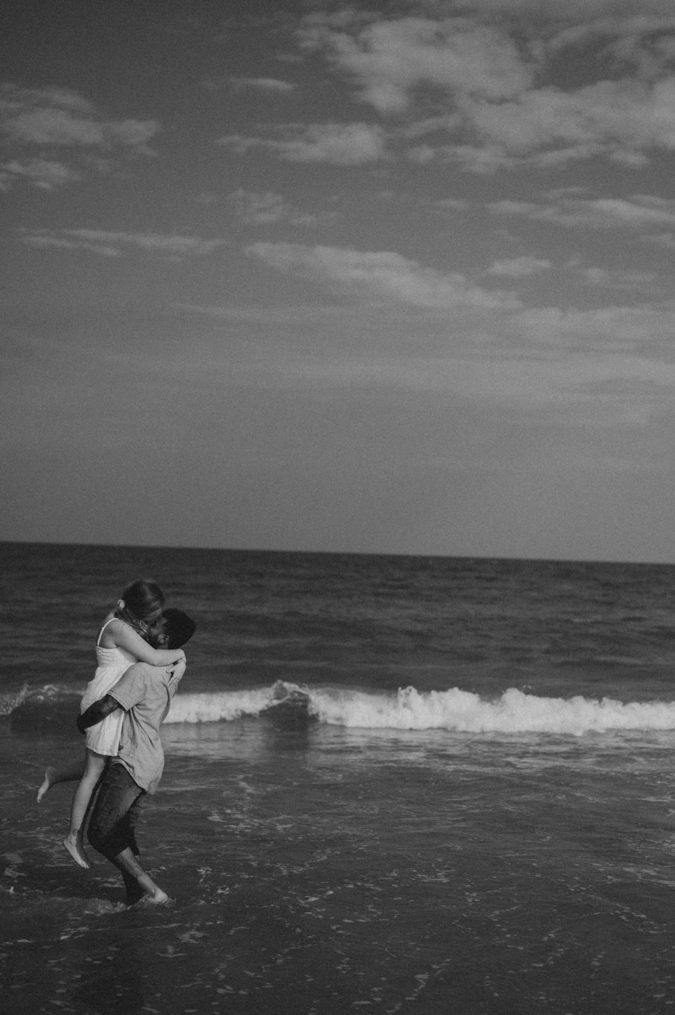 Black and white silhouette of people jumping in waves at the beach.