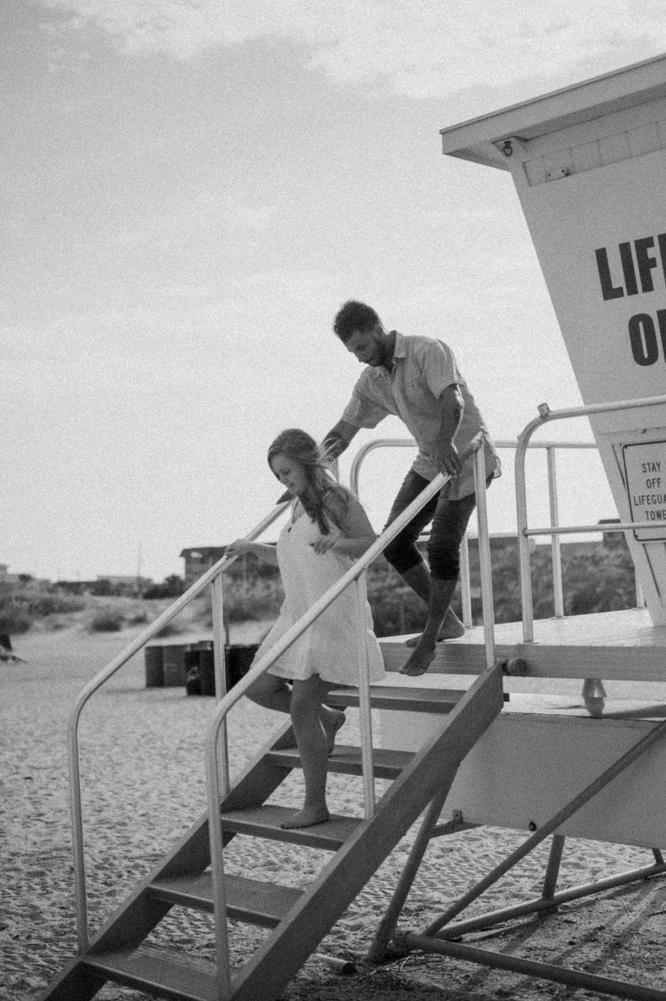 Black and white photo of people climbing stairs on a beach lifeguard tower.