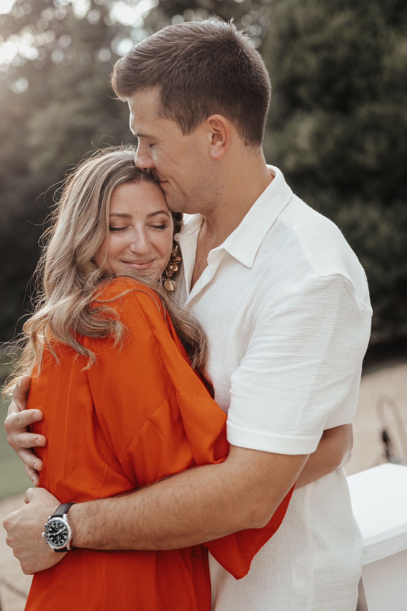A couple embracing outdoors, with one wearing orange and the other in white.